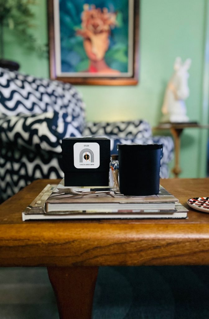 A cozy living room scene featuring a wooden coffee table adorned with a stack of books, a black candle, and a matching black mug.