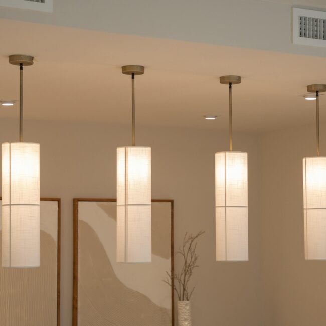 Set of four cylindrical pendant lights with textured shades and brass hardware, softly illuminating a neutral-toned interior by JohnRoss.