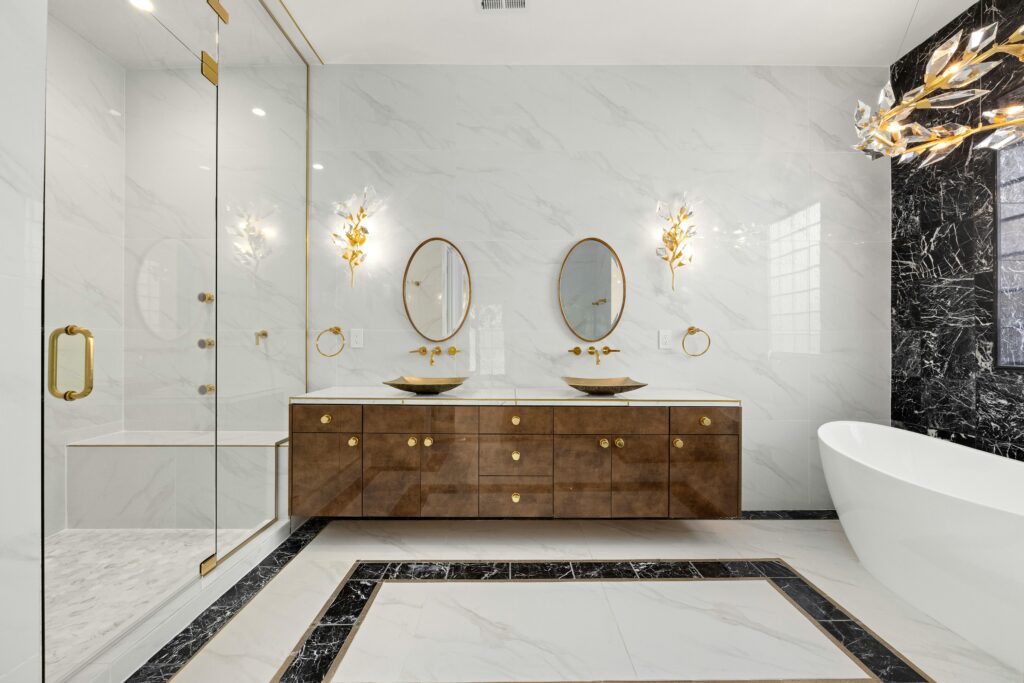 Luxurious marble bathroom with dual vanities, gold fixtures, and sculptural lighting — designed by JohnRoss for refined modern elegance.