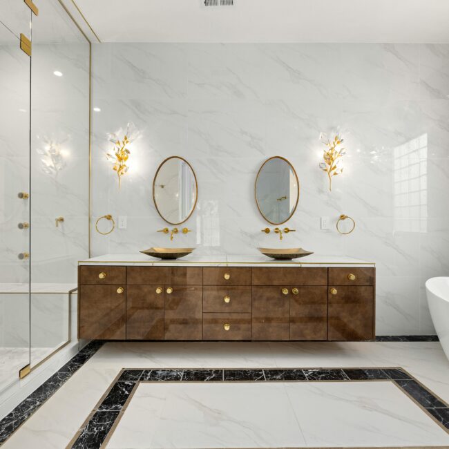 Luxurious marble bathroom with dual vanities, gold fixtures, and sculptural lighting — designed by JohnRoss for refined modern elegance.