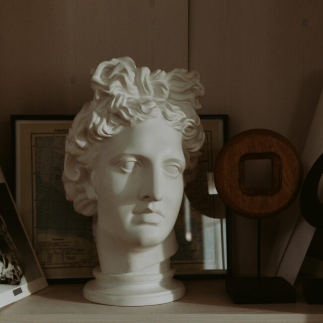 Shelf vignette featuring a classical bust, sculptural decor, and design books — curated by JohnRoss for an artful, collected aesthetic.