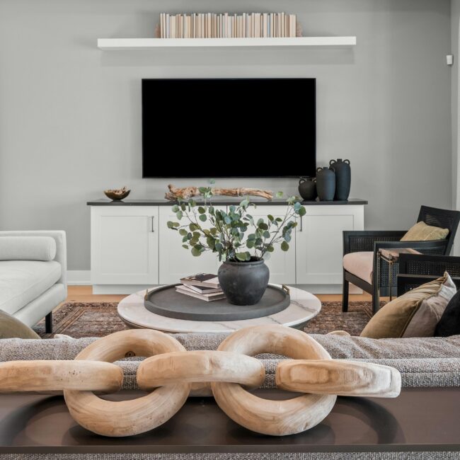 Stylish living room with neutral tones, sculptural wood chain decor, and a minimalist black-accented media console designed by JohnRoss.