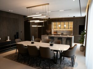Modern open-concept kitchen and dining area with minimalist lighting, marble surfaces, wood accents, and earthy tones designed for connection and calm.