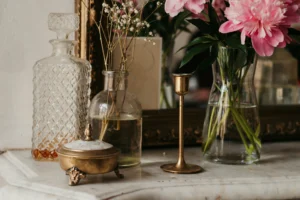 Styled marble mantel featuring a crystal decanter, antique brass candle holder, vintage glass vases with florals, and a framed mirror in the background.