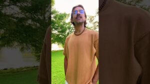 JohnRoss standing in a lush green park wearing sunglasses and a tan shirt, sharing insights on biophilic interior design and calming natural aesthetics.