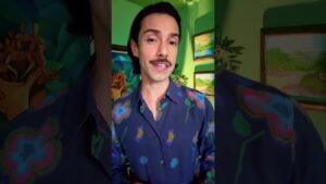 JohnRoss discusses color psychology in interior design while wearing a dark floral shirt, standing in a vibrant green room with tropical wall art.