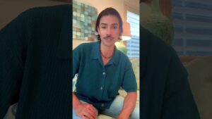 John Ross sits in a softly lit living room, wearing a textured teal shirt, discussing how tactile surfaces and sensory design affect emotional wellness.