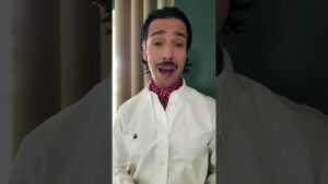 JohnRoss wearing a white button-down and red patterned neckerchief, standing indoors while explaining why interior design should reflect personal emotion over resale value.