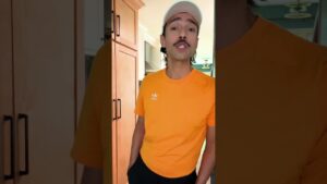 JohnRoss in an orange Adidas shirt and white cap, standing in a modern kitchen while sharing emotional interior design insights on why renovation should reflect your personal needs.